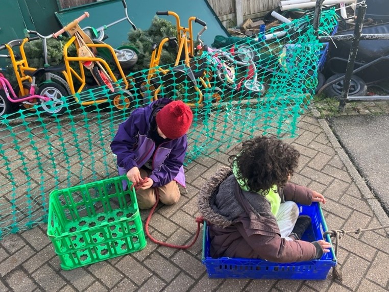 Child sitting in a blue crate and child playing with a green crate